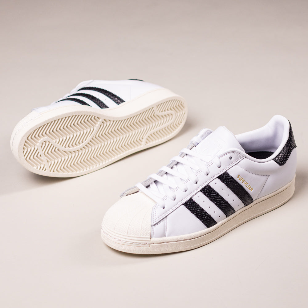 The Superstar ADV White Black KI5727 Adidas Skateboarding Suede Leather Shoes feature white suede, black stripes, gold SUPERSTAR text, and a herringbone-patterned sole that highlights their skateboarding design.
