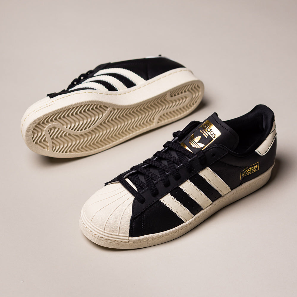 The KK5003 Black White Superstar 80 ADV Adidas Skateboarding Leather Shoes feature classic white stripes, shell toes, gold branding, and cream soles—an iconic choice for skaters, shown on a light gray background.
