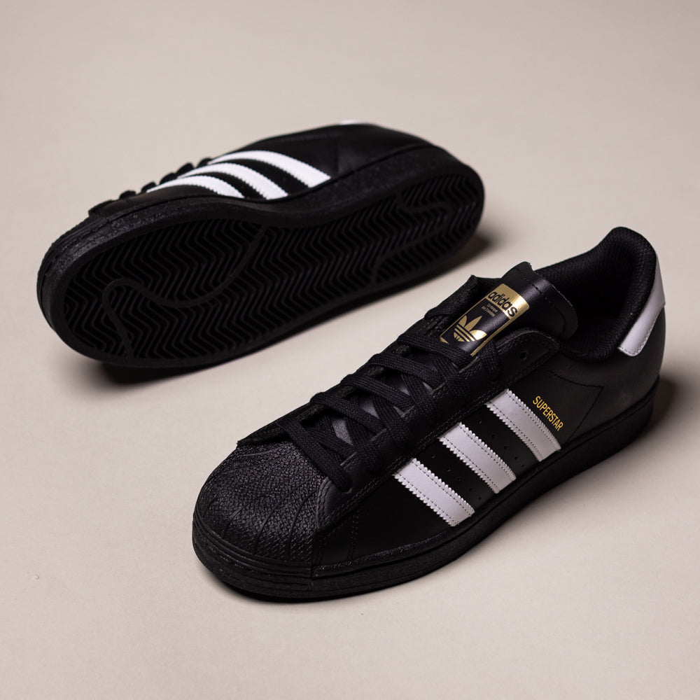 A pair of GW6931 Black White Superstar ADV Adidas Skateboarding Leather Shoes, featuring white stripes, gold branding, and black textured rubber soles on a light background. Iconic style perfect for skateboarding.
