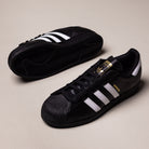 A pair of GW6931 Black White Superstar ADV Adidas Skateboarding Leather Shoes, featuring white stripes, gold branding, and black textured rubber soles on a light background. Iconic style perfect for skateboarding.