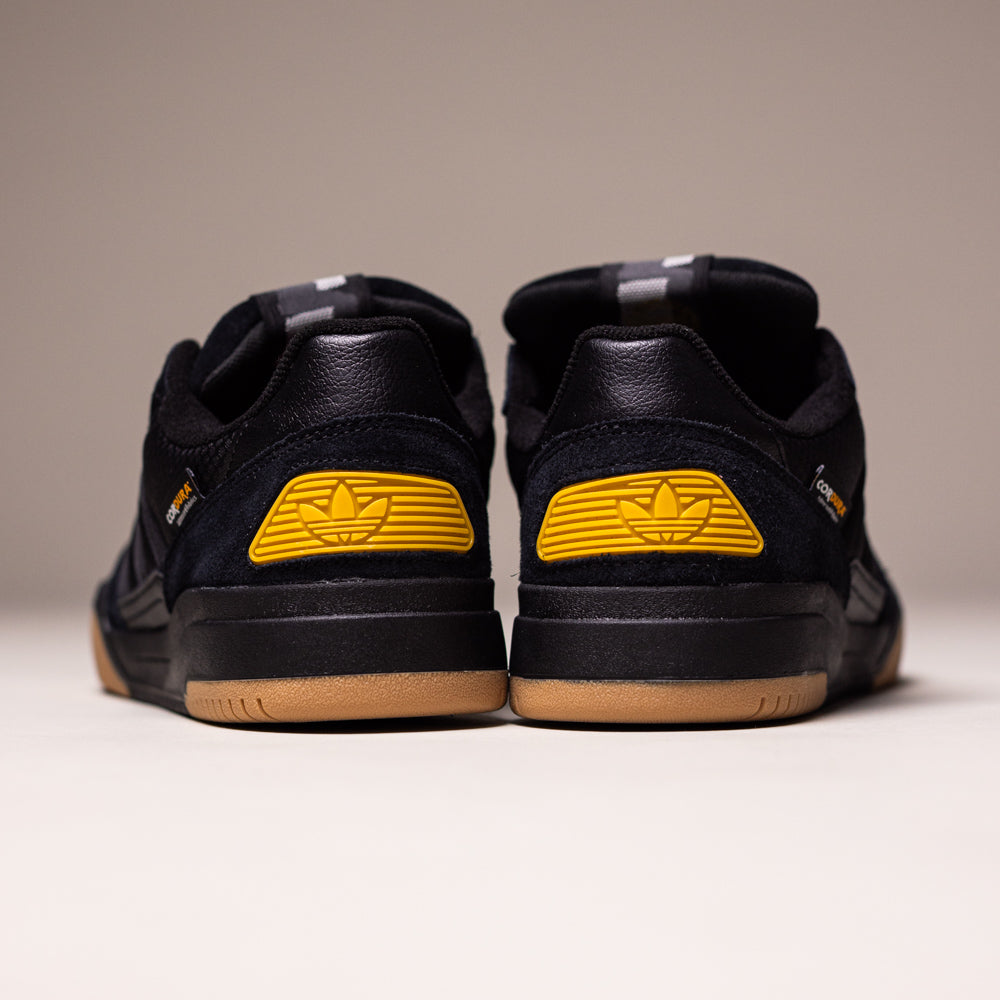 The KJ5054 Cordura Carbon Black Tekkira Cup Adidas Skateboarding Suede Shoes feature gum soles, yellow winged logo heel accents, and a durable suede upper. Shown from the back on a light surface with a neutral background.