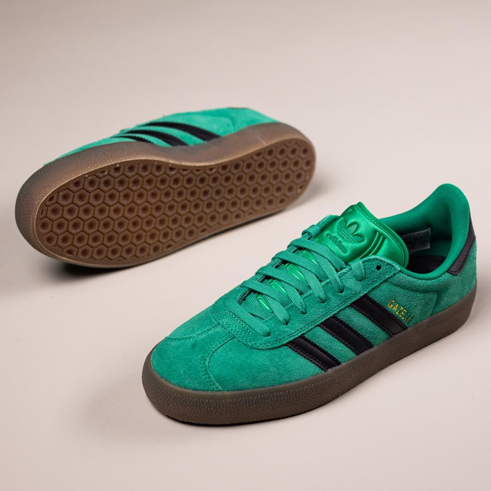 A pair of KI3206 Green Black Gazelle ADV Adidas Skateboarding Suede Shoes, featuring black stripes and brown rubber soles—one upright and one on its side—displayed on a light background, perfect for everyday adventures.