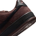 Close-up of the Air Force 1 Black Light Chocolate HM8517201 Nike SB Suede Skateboarding Shoe, showcasing a brown suede upper with a black sole and the word “AIR” embossed on the side. Visible stitching enhances the heel and upper, while signature Nike Air cushioning delivers superior comfort for skateboarding enthusiasts.
