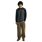 A man wearing a black and gray color-blocked Airmail Longsleeve IM5430060 Black Gray Skate Longsleeve T-Shirt SB Tee Skate Nike SB Skateboarding and olive-green pants.