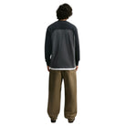 Back view of a person wearing a Nike SB Airmail Longsleeve IM5430060 Black Gray Skate Longsleeve T-Shirt over a white undershirt with baggy brown pants, offering durable comfort.