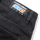 Close-up of the back pocket and waistband of Aleka Denim Jeans Flat Black Cash Only COD153202, featuring a black label with "CASHONLY COX JEANS" in white, blue, and red text, plus visible orange stitching details.