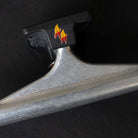 A close-up of the Andrew Allen Hollow Silver Black Standard INDY 149 Stage 11 Trucks Set of TWO, showcasing a black baseplate with yellow and red flame graphics against a dark background.
