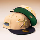 Two tan and black New Era 5950 fitted Houston Astros hats are stacked, each with a circle star logo and "The Original" Astrodome patch. One visor faces up, displaying its sticker—true standout pieces from 5950 Day.