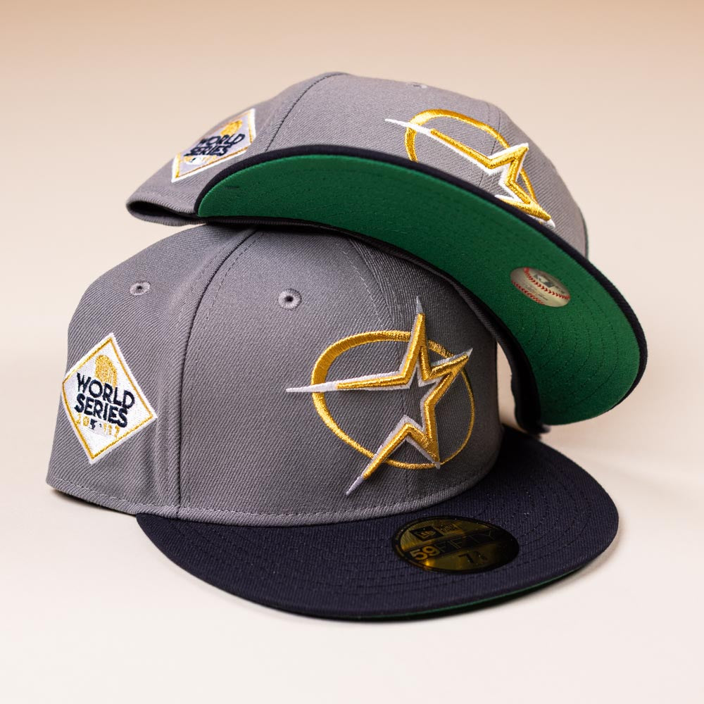 Two Gray Navy Circle Star Houston Astros New Era 5950 Day fitted hats feature star logos and black brims. One cap is stacked on the other, revealing a green underbrim—true batting practice style.