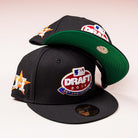 Two black, red, and blue Throwback 2015 Draft Day Houston Astros New Era 5950 Fitted hats are shown—one upright, the other leaning to display the green underbrim and team logos.