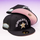 Two black Summer Nights Trilogy Houston Astros New Era 5950 Fitted caps are stacked; both show a silver and yellow H star, Houston text, side patch, gold brim sticker, and the lower cap features a pink undervisor.