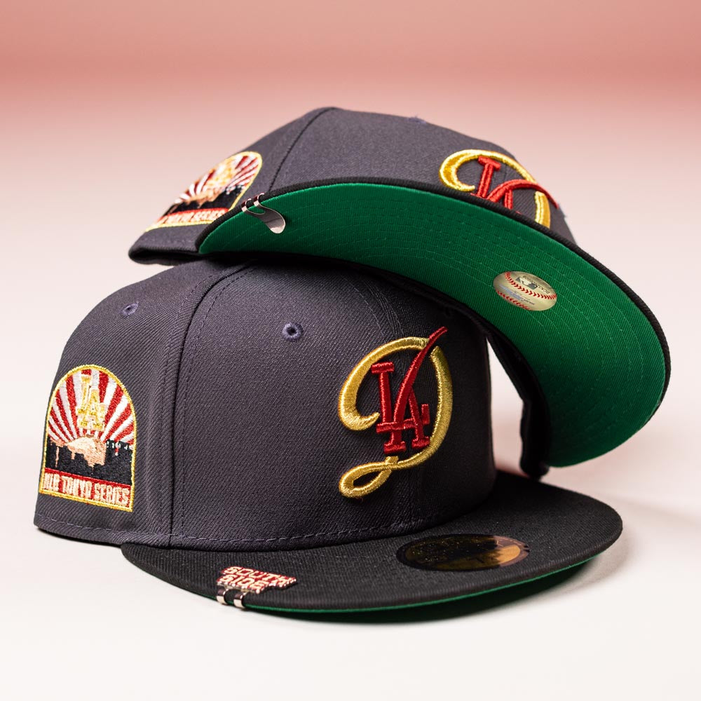 Two dark Bones Pack Los Angeles Dodgers 5950 Fitted New Era Hats with green brims, gold and red "LA" embroidery, a vintage "World Tokyo Series" patch, and brim stickers are stacked on a pink background.