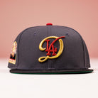The Bones Pack Los Angeles Dodgers New Era Hat 5950 Fitted features a dark gray design with a gold and red LA logo, red top button, stadium side patch, and is photographed against a pink background—ideal for Dodgers fans.