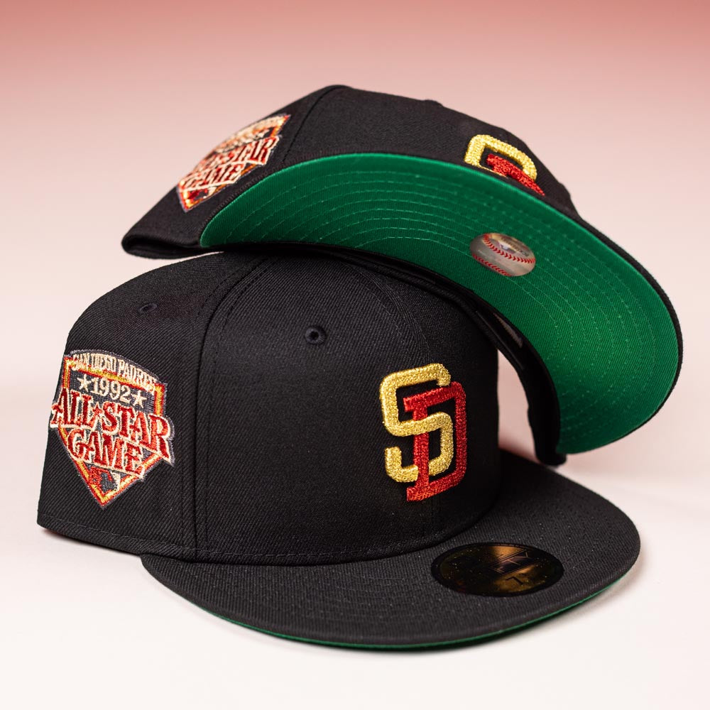 Two black Bones Pack San Diego Padres New Era Hat 5950 Fitted caps, featuring green brims, gold and red SD logos, and 1992 All-Star Game patches, are displayed against a gradient pink background.