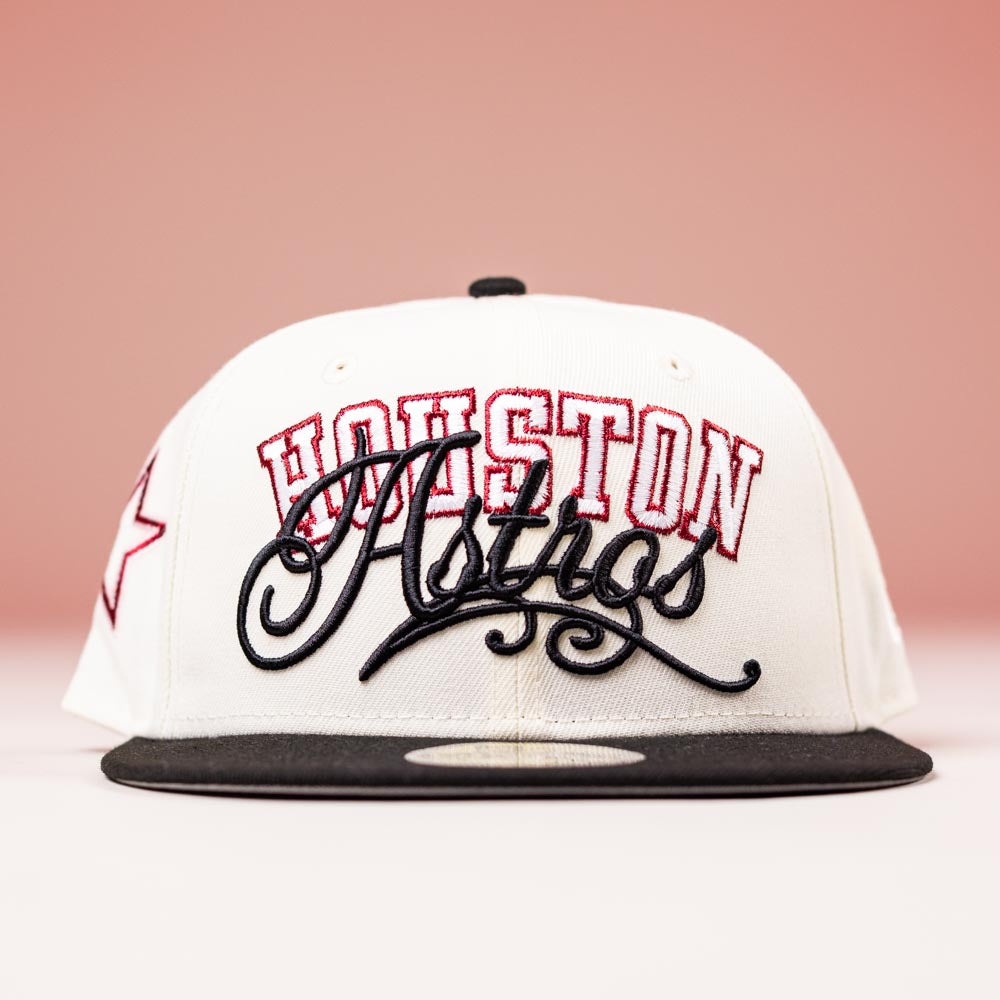 The D BOY Houston Astros New Era Hat 5950 Fitted features an ivory crown, black brim, and red-black embroidered logo, displayed against a pink background.