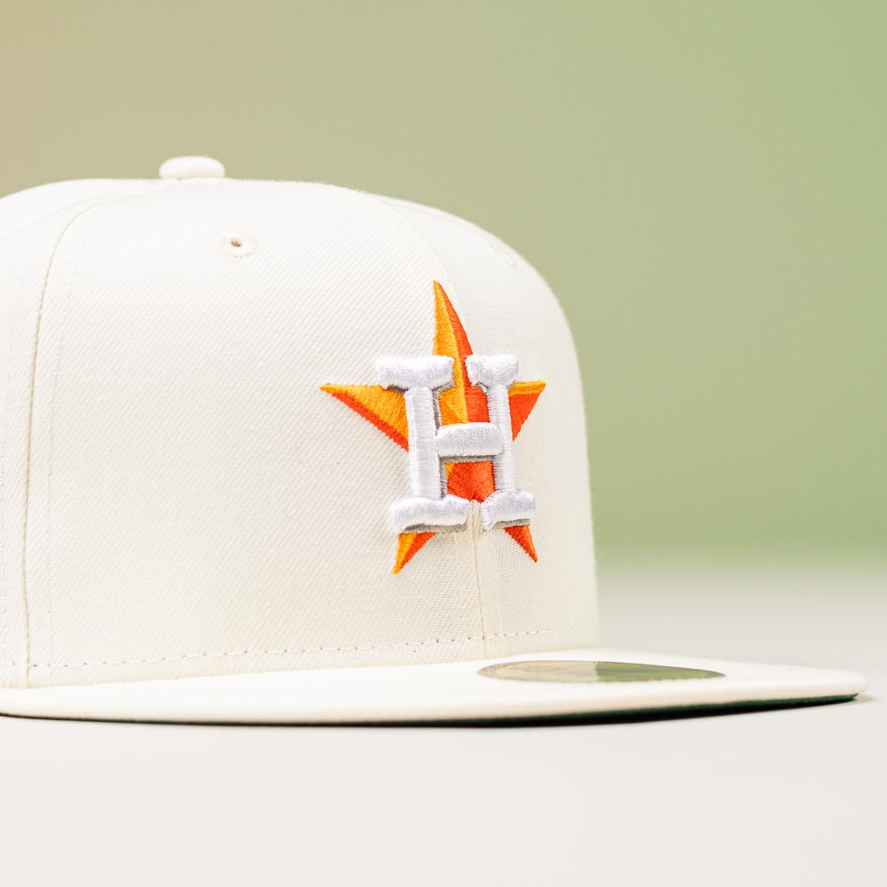 The Summer Days 2022 Houston Astros New Era Hat 5950 Day, featuring an orange star and white "H" on the front, is displayed on a neutral surface with a soft green background.