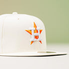 The Summer Days 2022 Houston Astros New Era Hat 5950 Day, featuring an orange star and white "H" on the front, is displayed on a neutral surface with a soft green background.