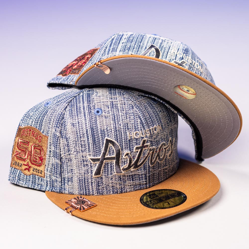 Two Bronze Denim 50th Houston Astros New Era 5950 Fitted hats with embroidered logos and a 50th anniversary patch on the side, one cap placed atop the other on a light surface.