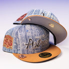 Two Bronze Denim 50th Houston Astros New Era 5950 Fitted hats with embroidered logos and a 50th anniversary patch on the side, one cap placed atop the other on a light surface.