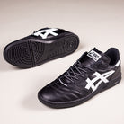 The Leggerezza Asics Black Bright White 1201B045 Leather Skateboarding Shoes are shown on a light background, with one upright and one on its side to highlight the white stripes, durable leather upper, breathable mesh, and textured sole.