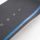 Close-up of the Atmosphere Switchblade 40 Landyachtz Complete Skateboard deck with black grip tape featuring white letters, showing layered wood edges and a blue accent stripe along the side.