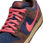 Close-up of the Baroque Brown Adobe Midnight Navy Dunk Low Pro HQ1625200 Nike SB Suede Shoes, featuring a brown suede overlay, blue base, pink Swoosh and laces, beige sole, and a brown tongue label with pink Nike SB text.