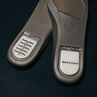Two gray insoles from the Ivory Sand Blue Void Dunk High Pro x Beyond IU4491100 Nike SB Skateboarding Shoes are shown. One insole displays the repeated phrase "Skateboarding is skateboarding," while the other features "Sports & Culture." Both have clear sections that reveal printed text, reflecting the iconic style of the Nike Dunk High basketball sneaker.
