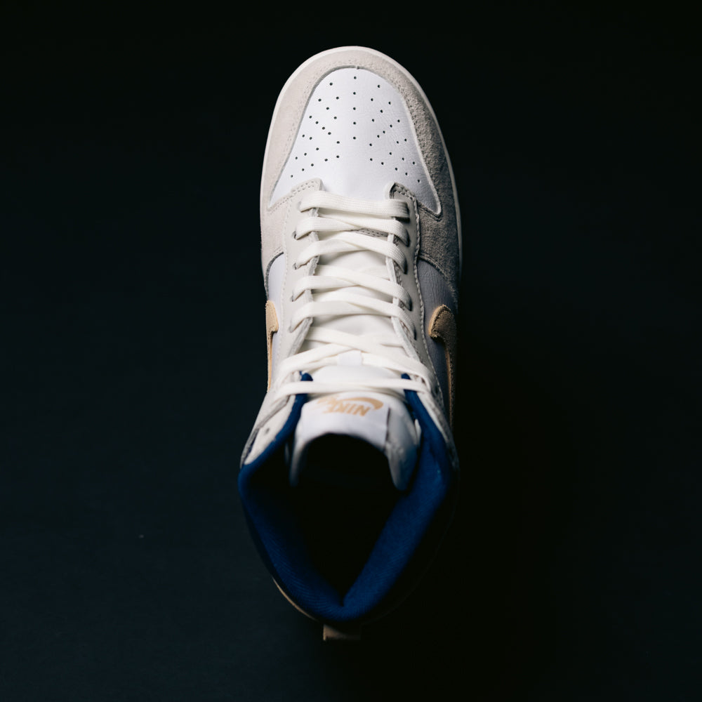 An Ivory Sand Blue Void Dunk High Pro x Beyond IU4491-100 Nike SB Skateboarding shoe is photographed from above against a dark background.