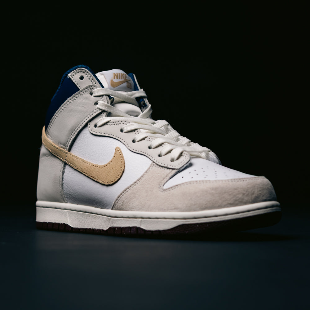 The Ivory Sand Blue Void Dunk High Pro x Beyond IU4491100 Nike SB Skateboarding Shoes feature a white and beige upper with a tan swoosh, dark blue accents, and white laces, displayed against a dark background.