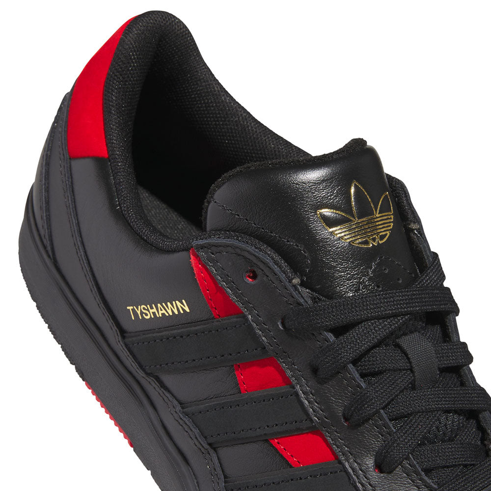 Close-up of the Black Black KK2981 Tyshawn II Suede Adidas Skateboarding Shoes, featuring red accents, gold Tyshawn branding, black laces, and a gold adidas logo on the tongue—an eye-catching design that stands out among modern skateboarding shoes.