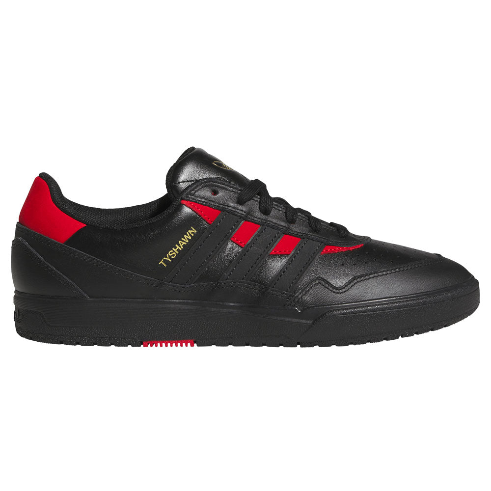 A black low-top skateboarding shoe, the adidas Tyshawn II Suede (Black Black KK2981) features subtle red accents, black laces, and three signature black stripes along the side. Gold “TYSHAWN” text appears near the stripes, and a bold red detail highlights the heel. Built for premium performance with a sleek black sole, these shoes combine style and function for skateboarders.