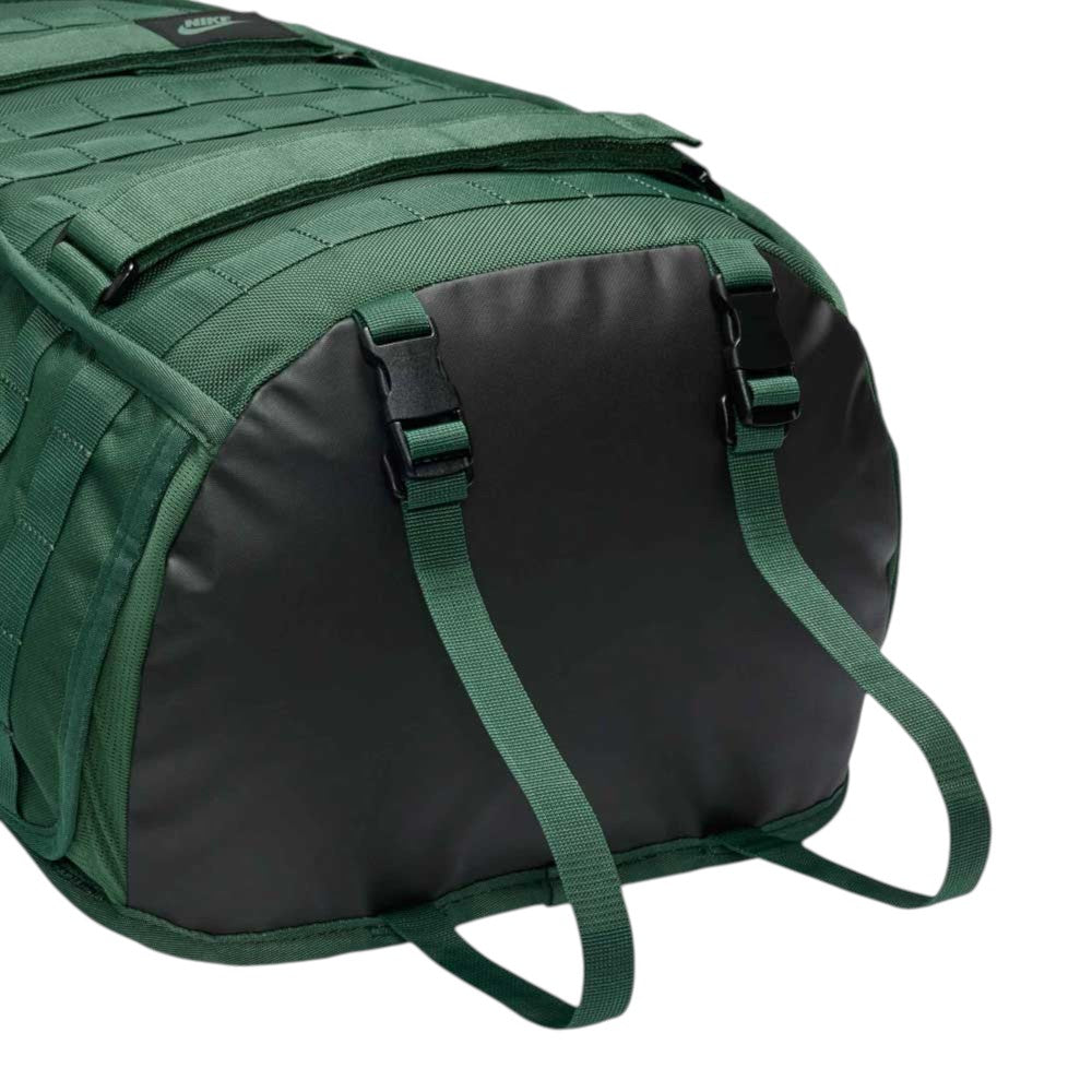 Close-up of the bottom end of the Black Fir FD7544323 Nike SB RPM Skate Backpack, featuring a green base with a black panel and two green adjustable straps attached with black buckles. This skateboard backpack showcases textured fabric, reinforced stitching, and a durable design crafted for skateboarding.