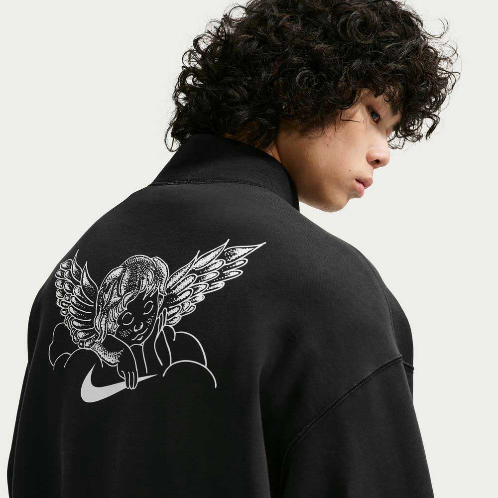 A person with curly hair wears the imported Black IM5463010 Skate 1/2 Zip Fleece Crew by Nike SB Skateboarding, featuring a white cherub with wings lounging on clouds graphic on the back. They look over their shoulder against a plain background. Machine wash recommended.