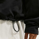 A close-up shows someone wearing a Black IM5463010 Skate 1/2 Zip Fleece Crew from Nike SB Skateboarding and white Nike sweatpants. Only part of the torso and one hand are visible; both items are machine washable.