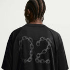 A person with braided hair is seen from the back, wearing a Black Jersey Tee IF1302010 Nike SB Skateboarding T-Shirt against a plain light background. The shirt features sweat-wicking fabric and chain link–styled number 02.