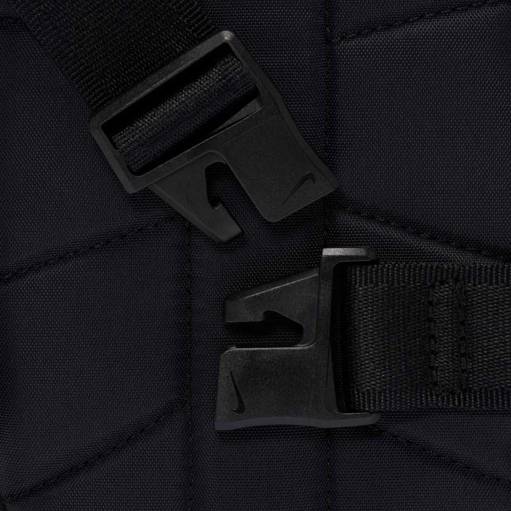Close-up of two black plastic buckle clasps attached to black straps, positioned against a quilted black fabric background of the Black Reflect Silver IQ1279010 Nike SB RPM Skate Backpack.