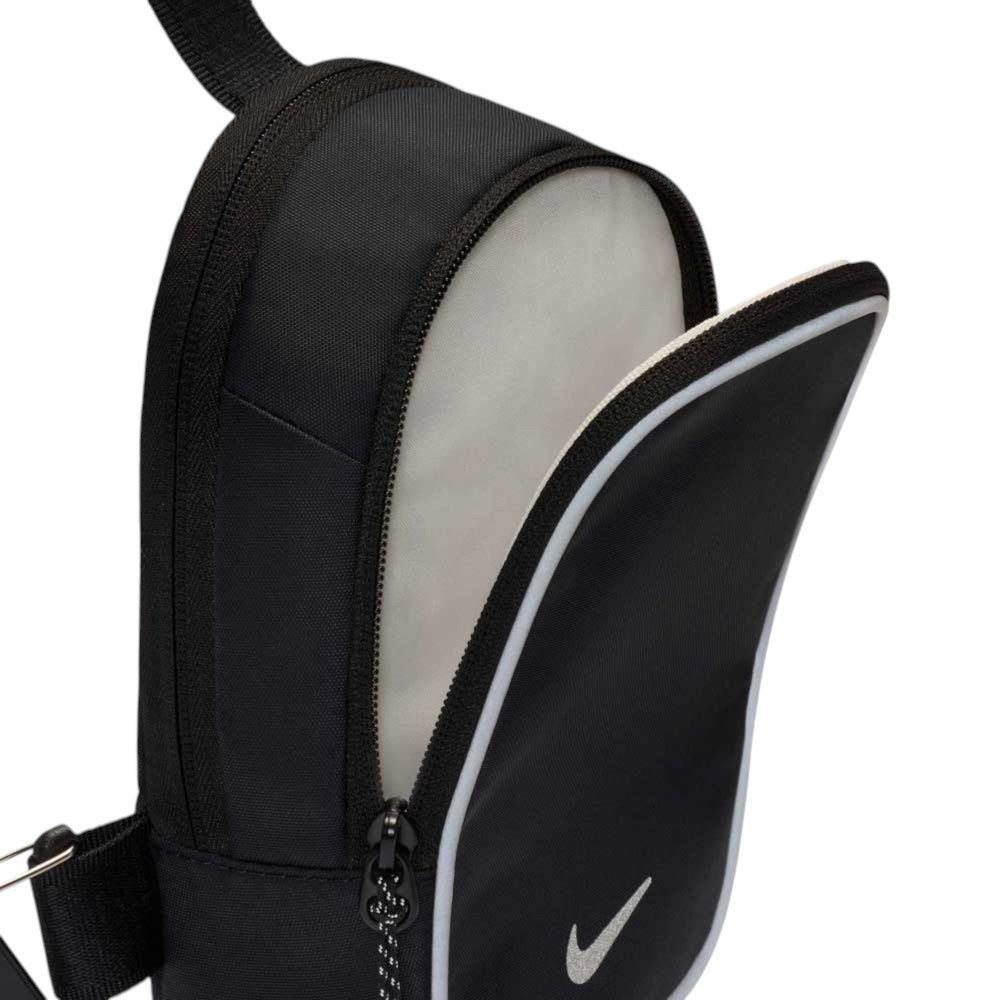 A close-up of the Black Reflect Silver IQ1279010 Nike SB RPM Skate Backpack showcases its black exterior with a white swoosh logo, partially unzipped to reveal a light gray interior. Both the zipper and strap are visible, highlighting this sleek and functional accessory—an ideal everyday choice for those who appreciate minimalist design.