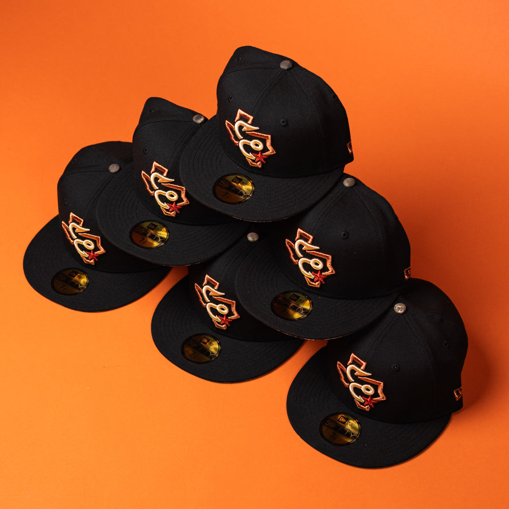 Six black baseball caps, including the eye-catching Hooked in Camo Corpus Christi Hooks New Era Hat 5950 Fitted with its distinctive orange and gold logo, are arranged in a pyramid shape on an orange background. Each cap features a gold sticker on the bill for an authentic finish.
