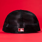 A Black Scarlet Trucker Houston Cougars New Era Hat 5950 Fitted, shown from the back with a small white and red MLB logo on black mesh, stands out against a red background—ideal for fans of the New Era Hat and Houston Cougars.