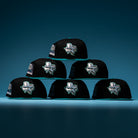 Six Silver Lining Black Teal 2000 Houston Astros New Era 5950 fitted hats are stacked in a pyramid formation, each featuring the signature star and state outline logo on the front. The bold black and teal colorway stands out strikingly against a blue gradient background.