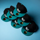 Six Silver Lining Black Teal 2000 Houston Astros New Era 59FIFTY fitted hats, each featuring Chrome Black gold stickers and embroidered white Houston Astros logos, are arranged in a pyramid shape on a light blue background.