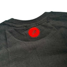A close-up of the back neck on the Bronze 56K x Ice Cream Wunning Dog Tee Black displays a small red starburst graphic with an "R" and text printed directly on the fabric.