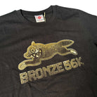 The Bronze 56K x Ice Cream Wunning Dog Tee Black features a stylized metallic gold dog with sharp teeth, inspired by the Dog Tee aesthetic, and "BRONZE 56K" printed below the graphic.
