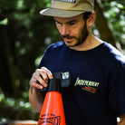 A man outdoors, surrounded by greenery and embodying the Built to Grind spirit of Independent Trucks, holds the Built to Grind Independent Phone Cone while wearing an Independent Truck Co shirt and cap.