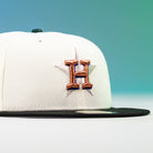 The Houstatlantavegas Chrome Black Green ASG Houston Astros New Era 5950 Fitted Hat, featuring a gold embroidered H over a star on a white crown with black brim, is shown against a blue and green gradient background.