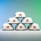Six Houstatlantavegas Chrome Black Green ASG Houston Astros New Era Hat 5950 Fitted caps, each with the team’s iconic H logo, are stacked in a pyramid against a blue and green gradient background. Perfect for dedicated Astros fans.