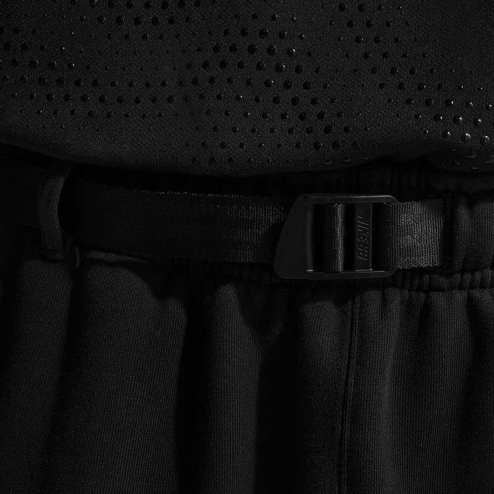 Close-up of a person wearing the Ishod Cargo Pant Sweatpant Black IF0659010 Nike SB with an elastic waistband and black plastic buckle belt, paired with a black perforated top.