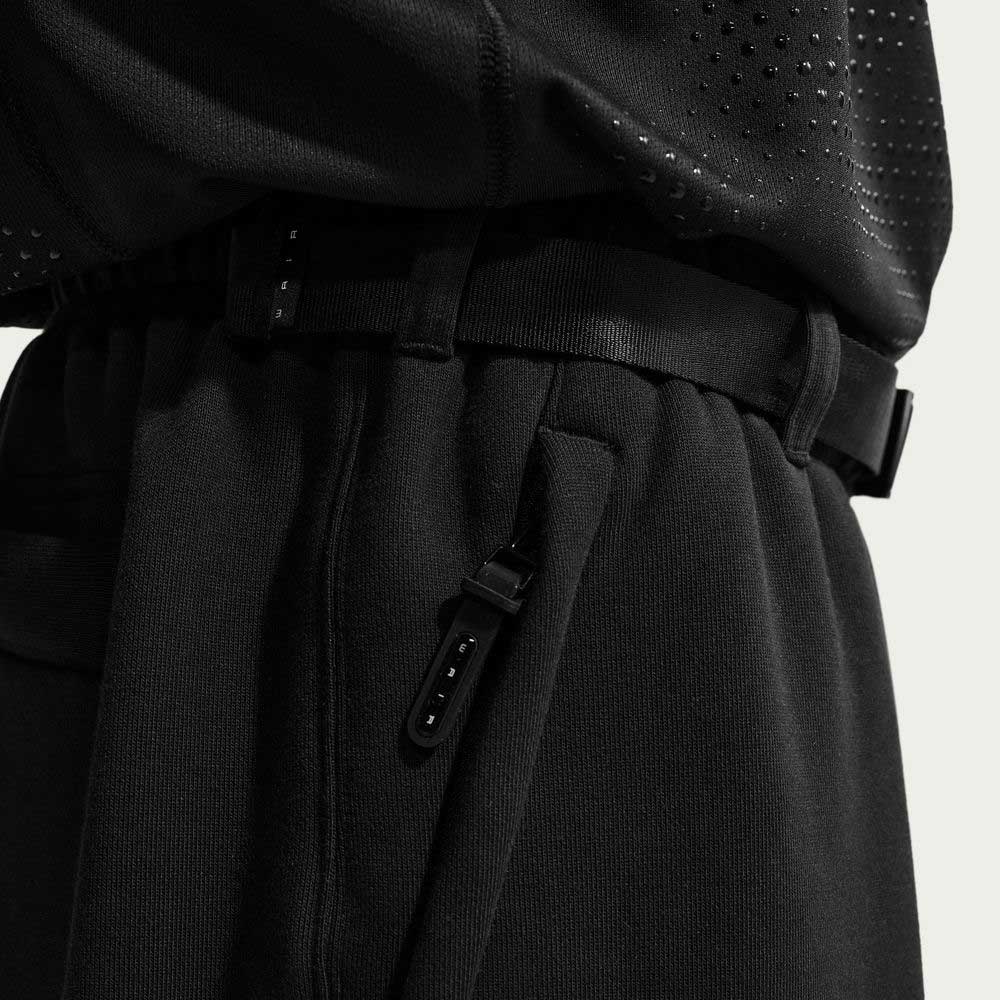 Close-up of a person wearing the Nike SB Ishod Cargo Pant Sweatpant Black IF0659010, featuring an adjustable strap, matching black perforated top, highlighted waistband detail, and heavyweight brushed fleece fabric.