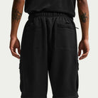 A person shown from the back wears black Ishod Cargo Pant Sweatpant Black IF0659010 by Nike SB and a black top. The pants feature large back pockets, and both tattooed forearms are visible.