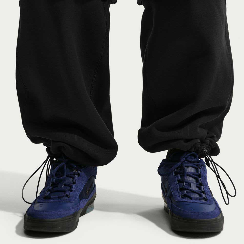 A person wearing Ishod Cargo Pant Sweatpant Black IF0659010 by Nike SB with drawstring ankles and dark blue sneakers, standing on a light background.